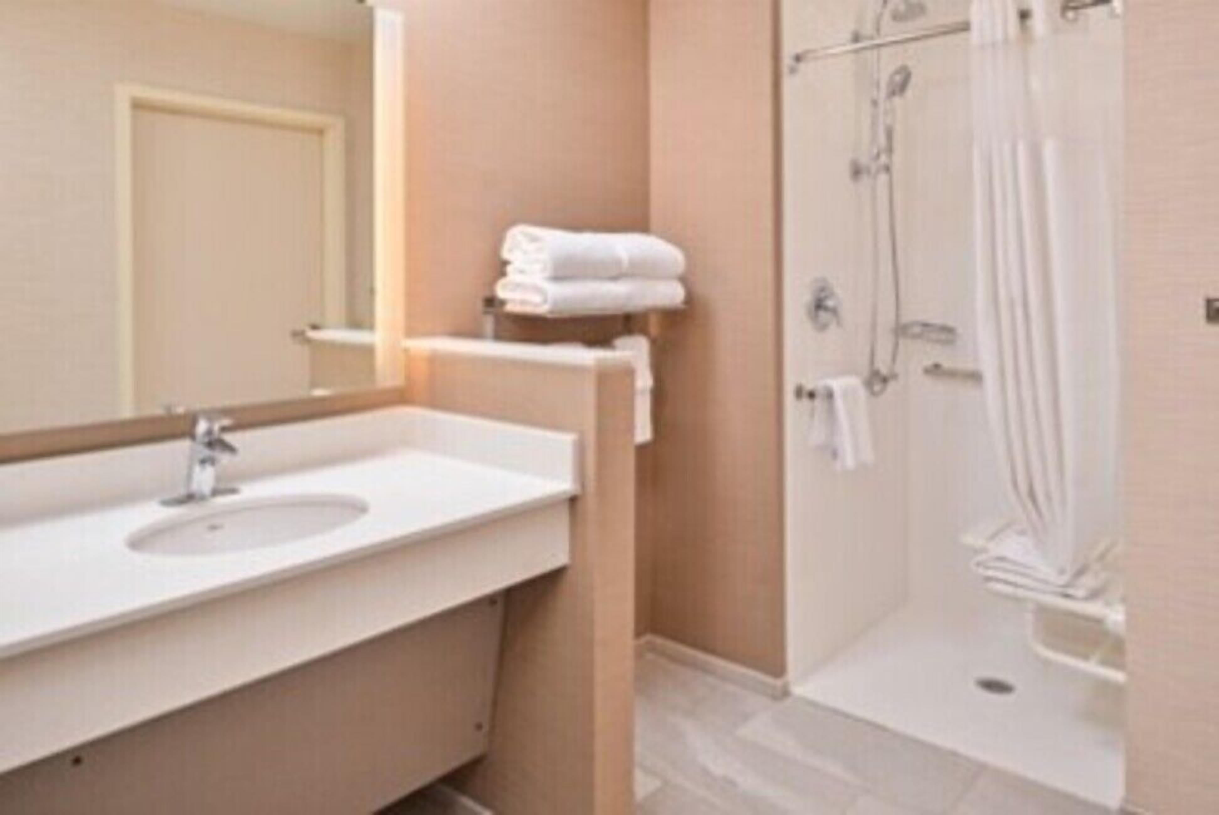 Een badkamer met een wastafel, spiegel, handdoekrek en douche.