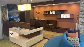 A reception area with a desk, chairs, and a colorful carpet. There is a wall with a 'Connect & Print' sign and a shelf with decorative items.
