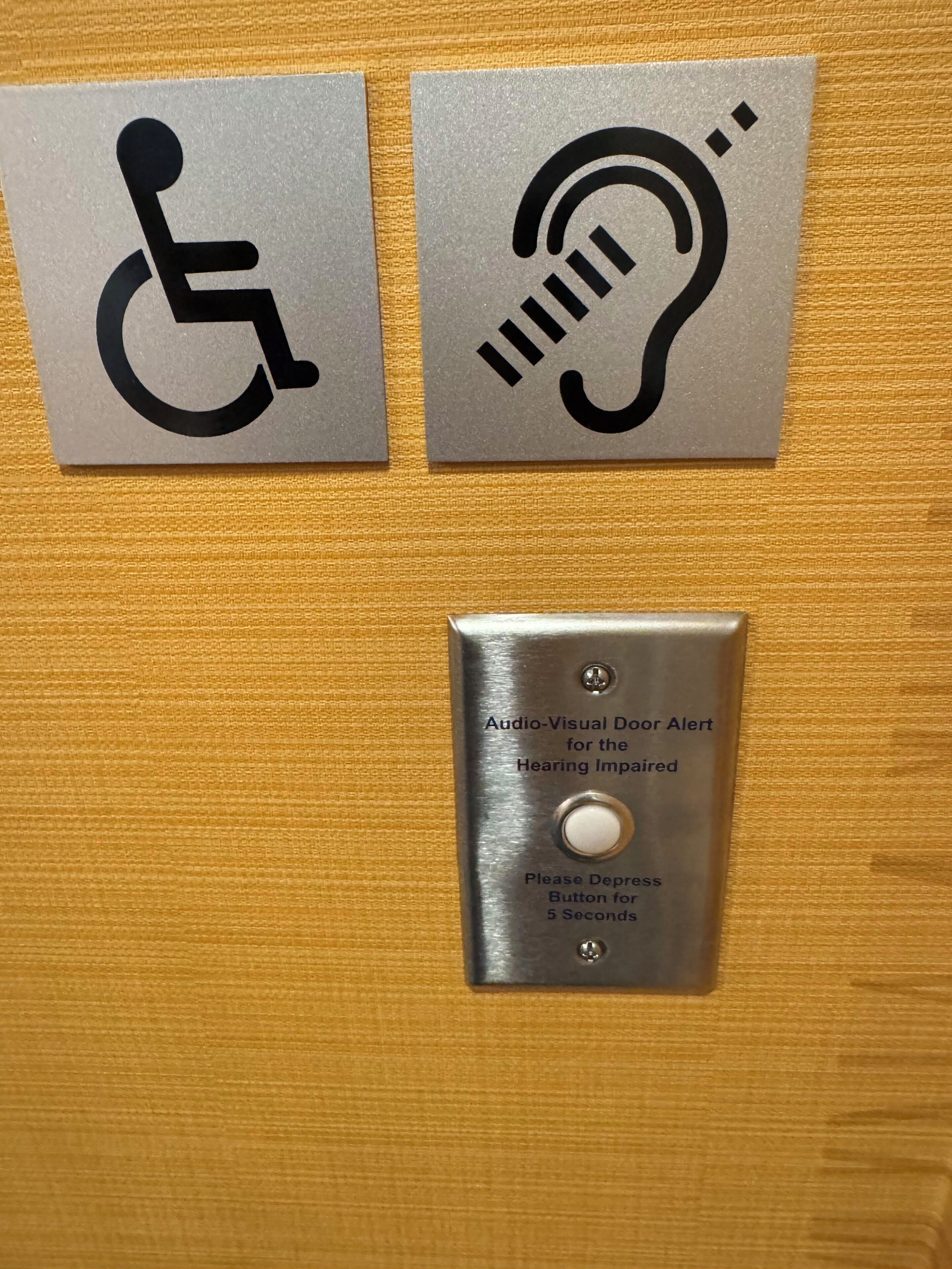 Deux panneaux indiquant les aménagements facilitant l’accès : un symbole représentant un fauteuil roulant et un bouton d’alerte audiovisuel pour les personnes malentendantes.