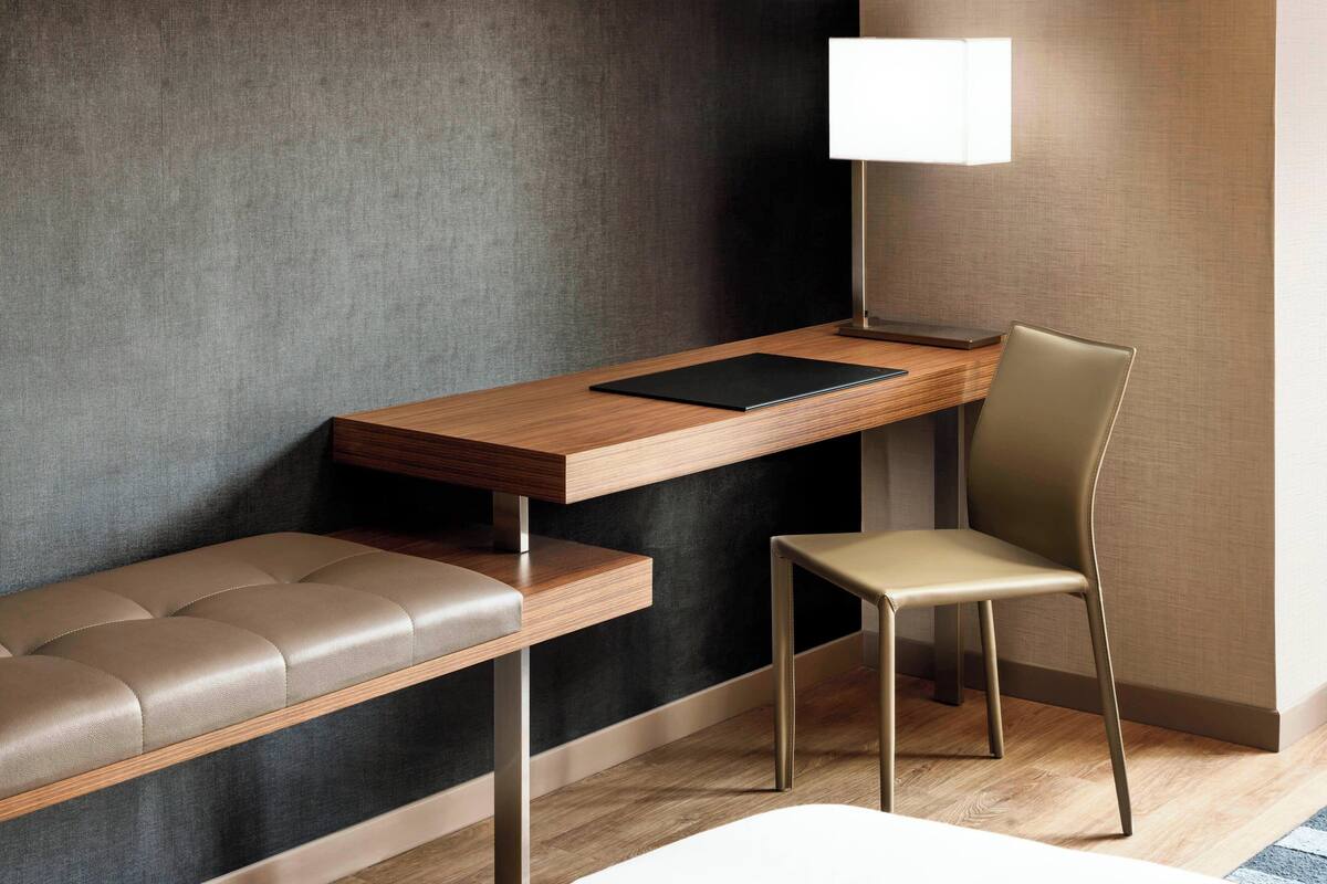 Una habitación moderna con un escritorio de madera, un banco acolchado, una silla y una lámpara.