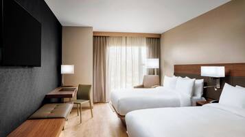 A hotel room with two beds, a desk, a chair, and a TV.