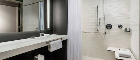 A modern bathroom with a large mirror, two sinks, a shower with a glass door, and a small table with a towel.