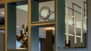 A modern interior with a glass partition, a metallic sculpture, and a ceiling with light fixtures.