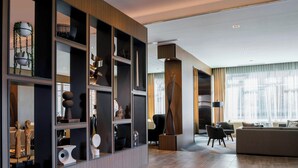 Uma sala de estar moderna com um sofá seccional, uma mesa de centro e uma lareira. Há prateleiras com objetos decorativos e uma janela grande com cortinas.