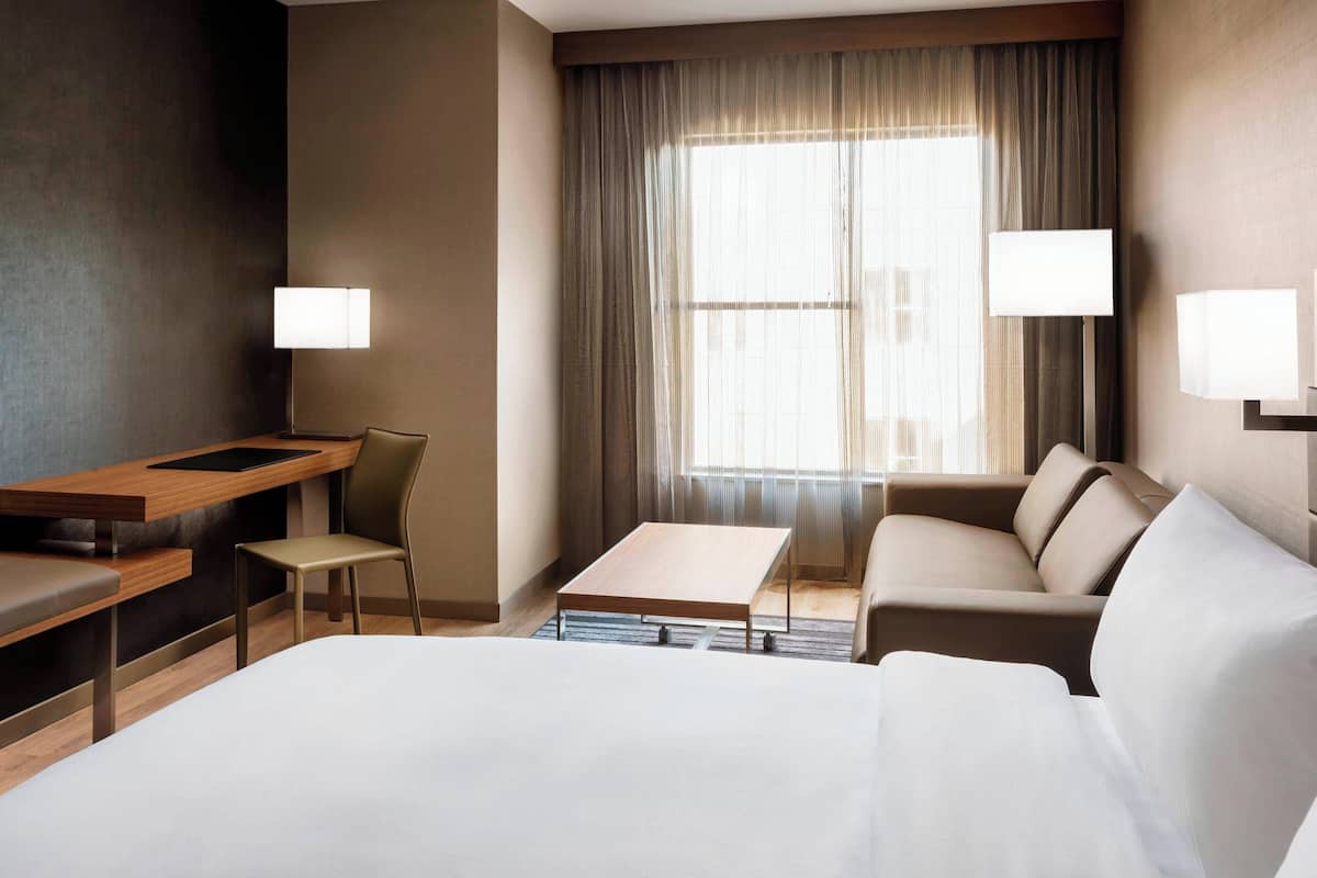 Una habitación de hotel con cama, escritorio, silla, sofá y ventana con cortinas.