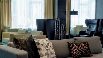A modern hotel lobby with a gray sofa adorned with patterned cushions, a black armchair, and tall, dark vases.