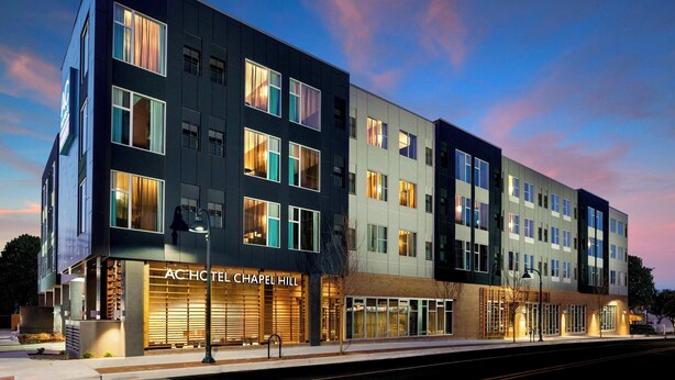 Um hotel moderno com fachada plana, grandes janelas e uma placa com a inscrição "ACHOTEL CHAPEL HILL".
