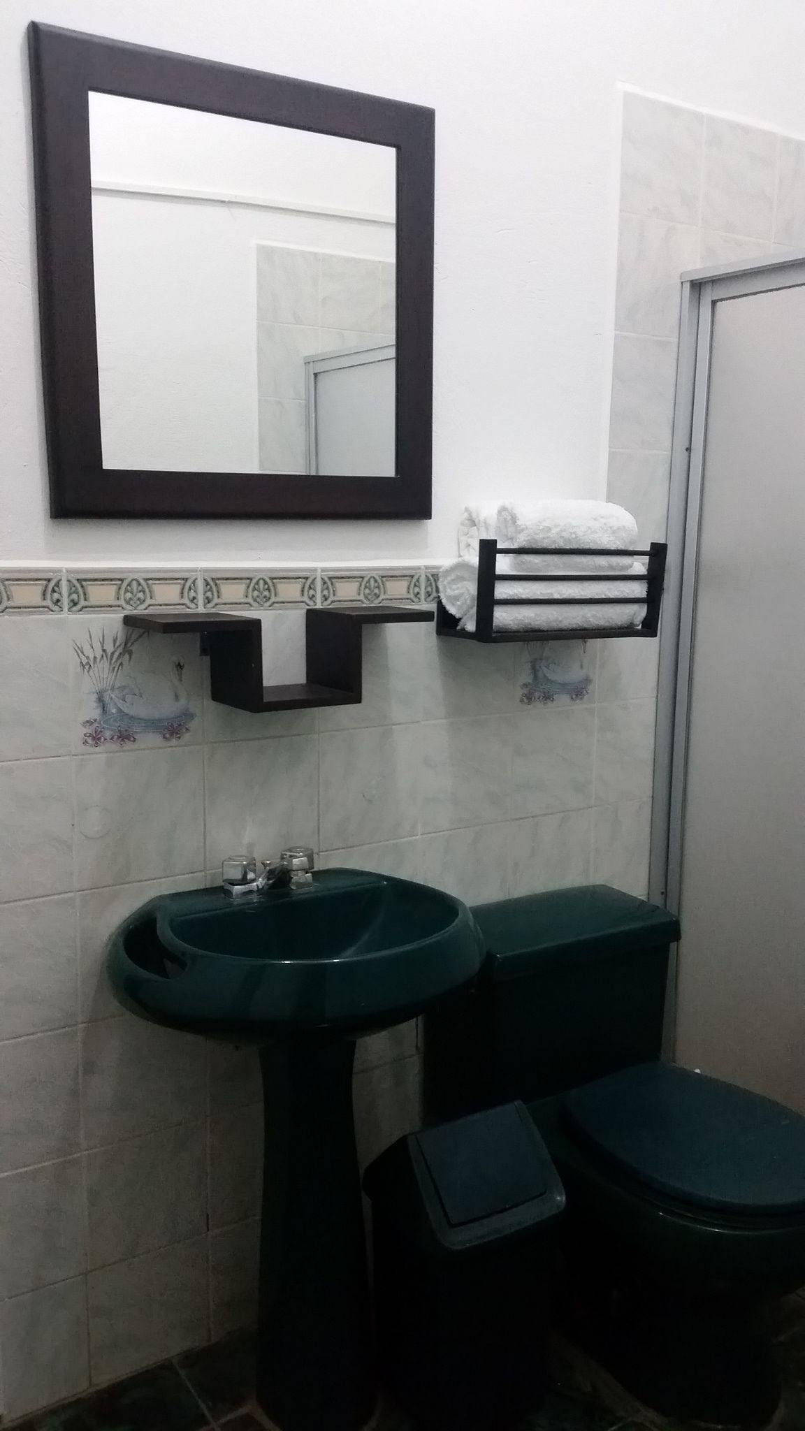 Un baño con lavamanos pedestal, inodoro, perchero y espejo.