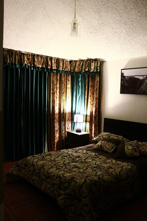 A bedroom with a bed, a nightstand, a lamp, and curtains. - Hotel Rubus (Puembo)