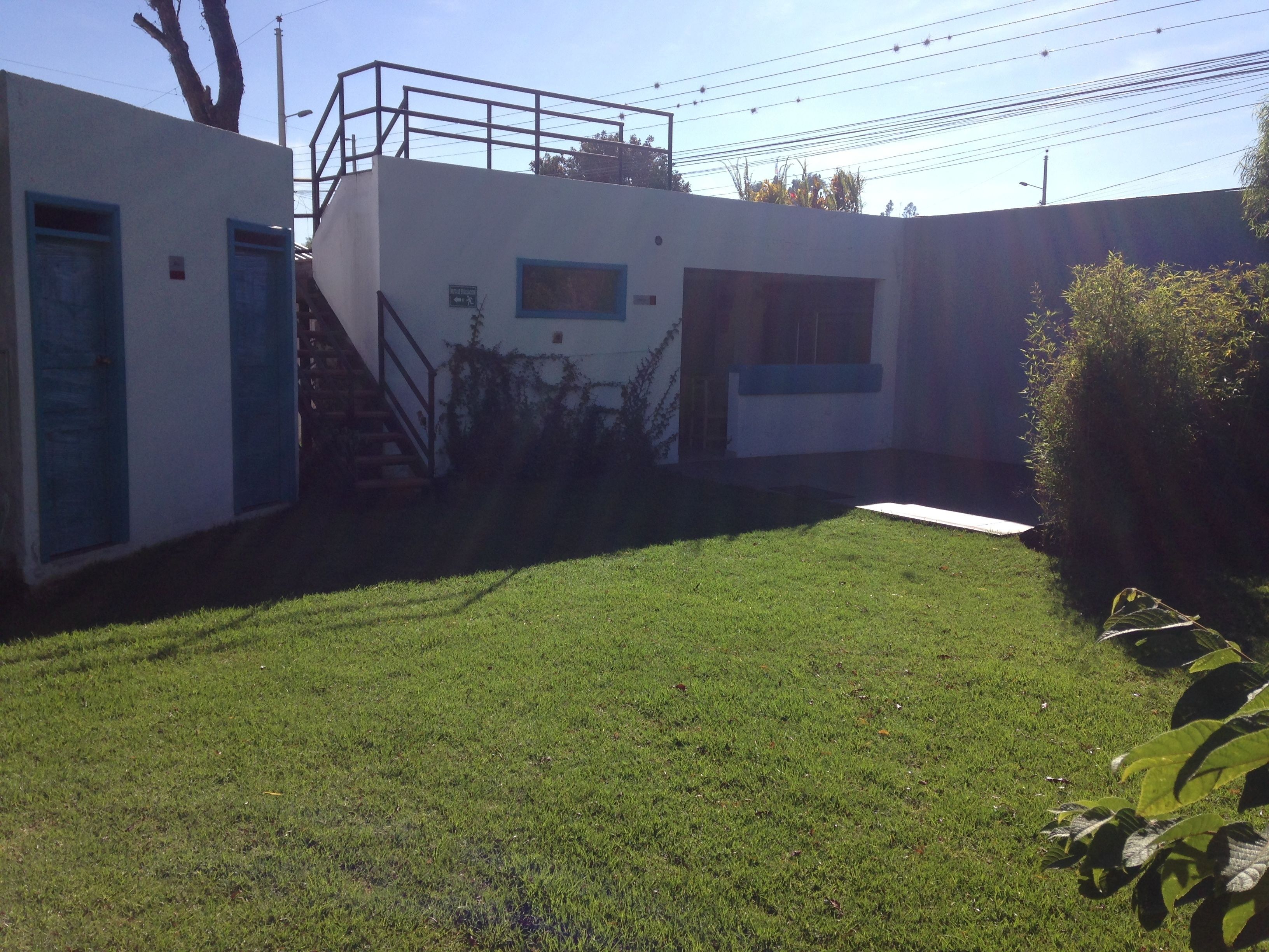 A building with a flat roof, a staircase leading to a second level, and a small garden area with grass and a pathway.