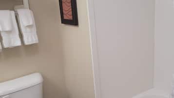 A bathroom with a toilet, a towel rack with folded towels, and a framed picture on the wall.