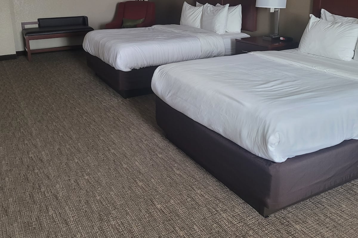 A hotel room with two beds, a desk, a chair, and two lamps.