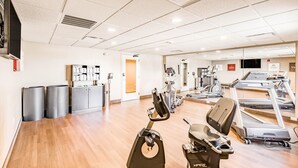 Academia com máquinas de cardio, um banco de peso e um espelho.