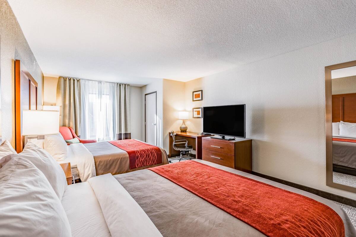 A hotel room with two beds, a desk, a TV, and a mirror.