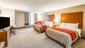 Quarto de hotel com duas camas, uma escrivaninha, televisão e janela com cortinas.