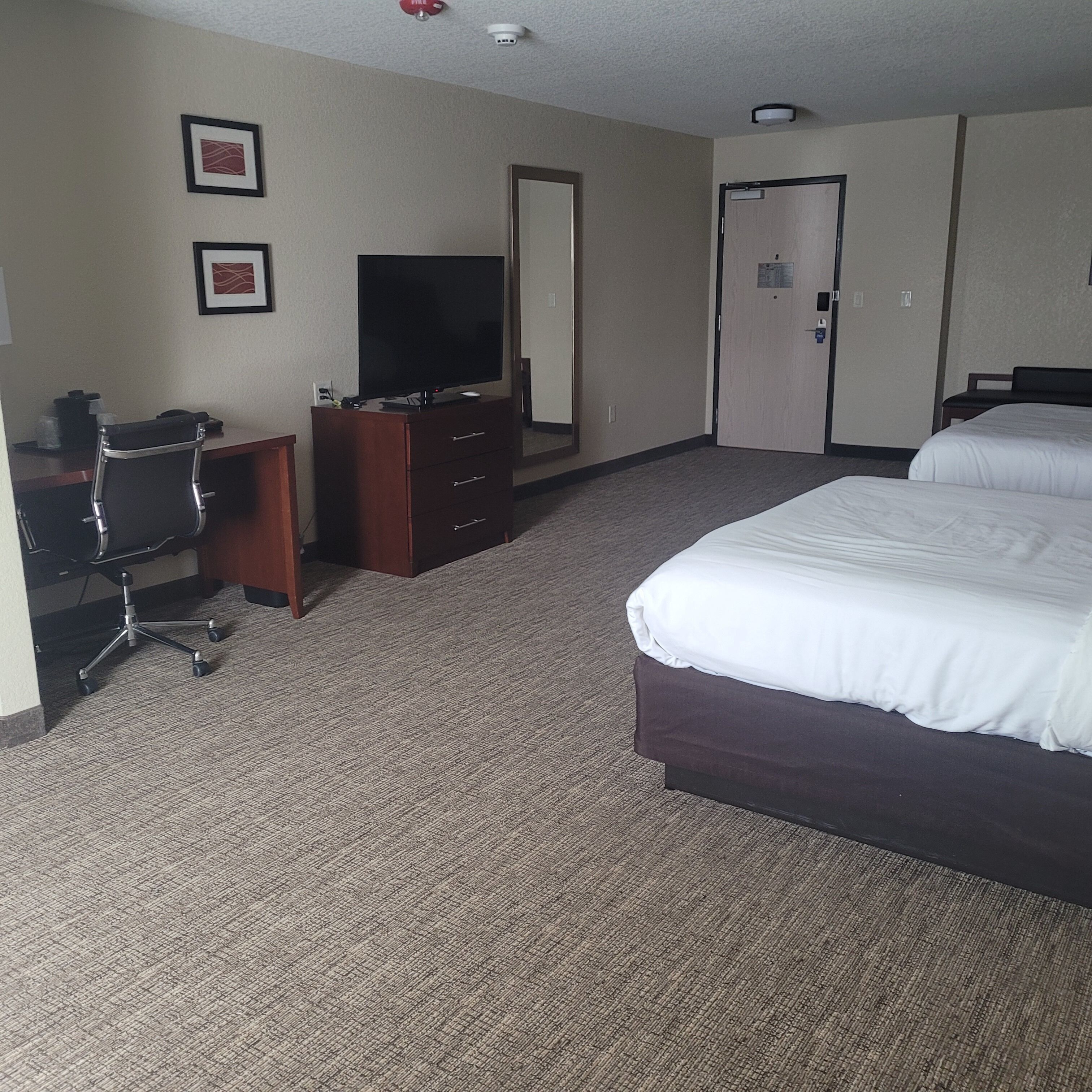 A hotel room with a large bed, a desk with a computer, a television, and a door.