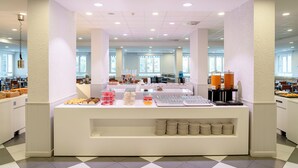 Un área de bufé con una variedad de alimentos y bebidas, una estación de café y un espacio de descanso con mesas y sillas.