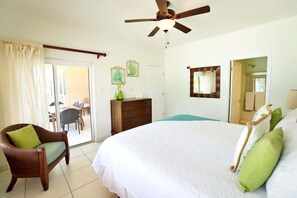 Een hotelkamer met een groot bed, een houten stoel, een dressoir, een plafondventilator en een deur die uitkomt op een balkon.