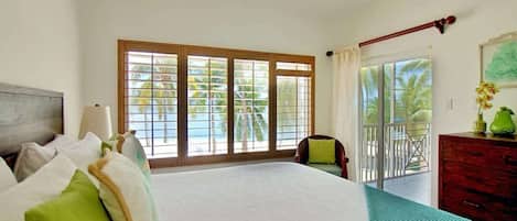 Un dormitorio con una cama grande, un ventilador de techo, vistas al exterior a través de una puerta corrediza de vidrio y un aparador de madera.