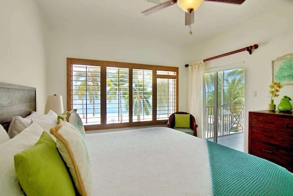 A bedroom with a large bed, a ceiling fan, a view of the outdoors through a sliding glass door, and a wooden dresser.