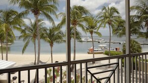 A balcony with a view of a beach, palm trees, and a marina with boats.