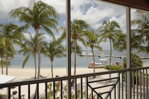 A balcony with a view of a beach, palm trees, and a marina with boats.