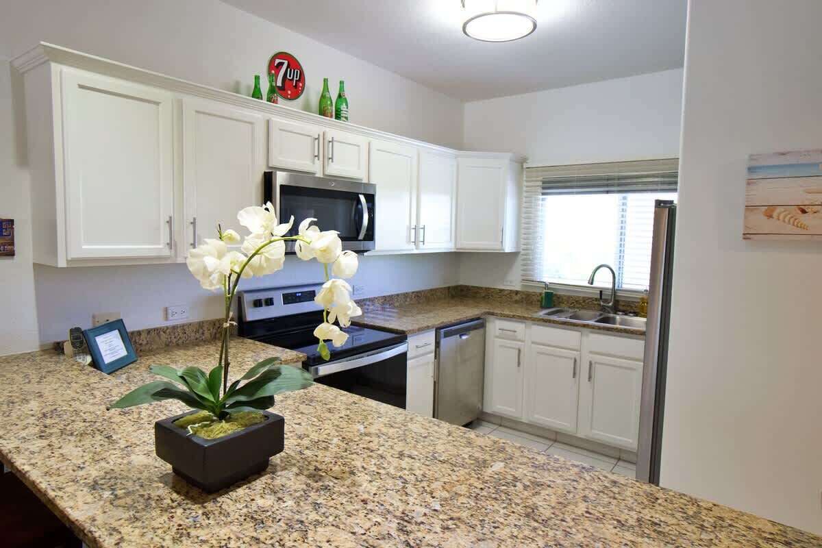 A kitchen with white cabinets, a granite countertop, a microwave, a dishwasher, and a potted orchid.
