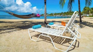 A beach with a hammock, lounge chairs, and a pool.