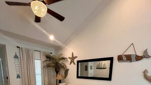Sala de estar com sofá seccional, ventilador de teto, espelho grande e arte decorativa nas paredes.