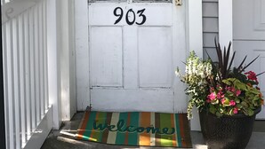 Una puerta blanca con el número 903, un adorno de flores y un felpudo.