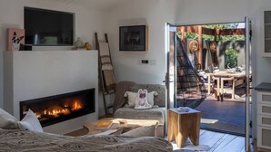 A cozy living room with a fireplace, a sofa, a small table, and a view of an outdoor deck with a dining area.