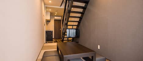 Un pasillo estrecho con una mesa de madera y un banco, una escalera y una pequeña zona de kitchenette.