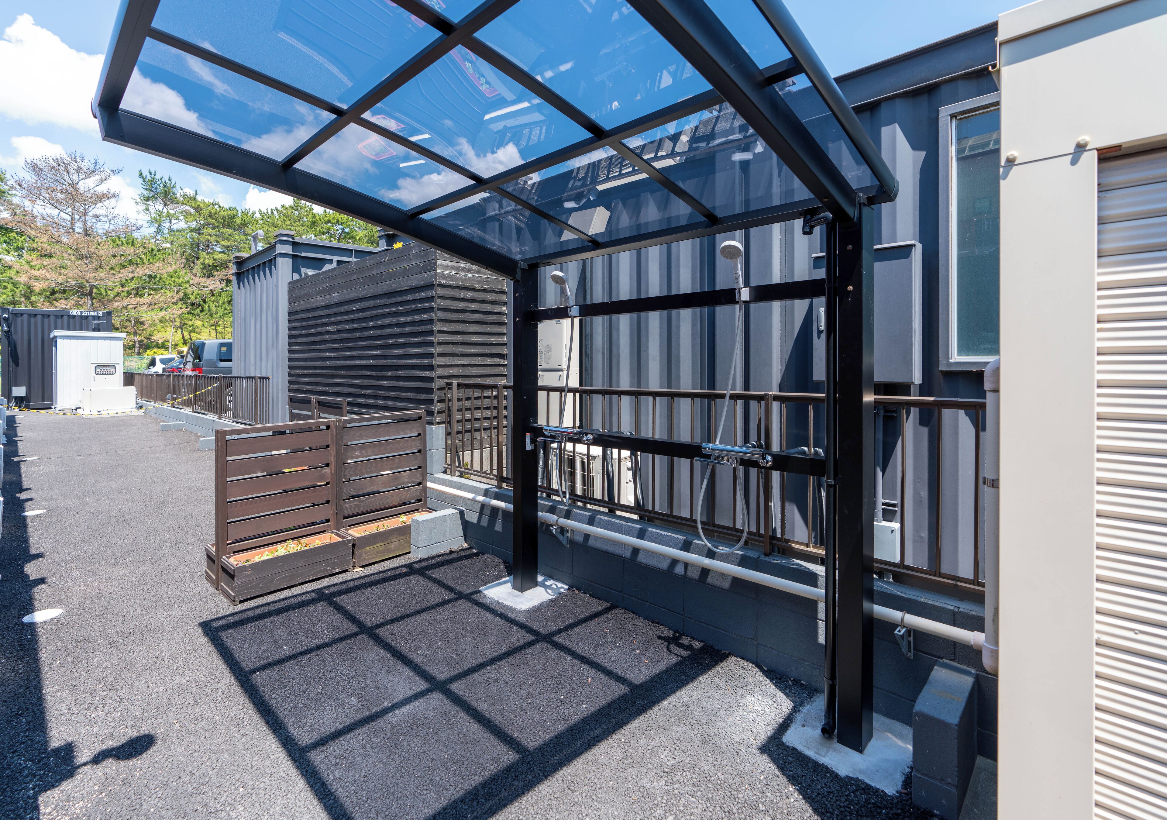 A covered parking area with a metal gate, a concrete floor, and a building with a garage door.