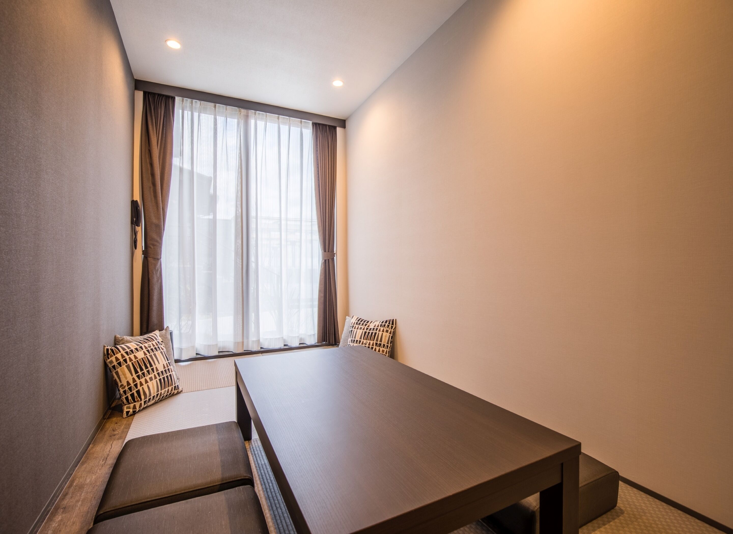 A modern hotel room with a large bed, a wooden table, and a window with sheer curtains.