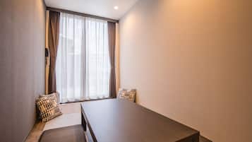 A modern hotel room with a large bed, a wooden table, and a window with sheer curtains.