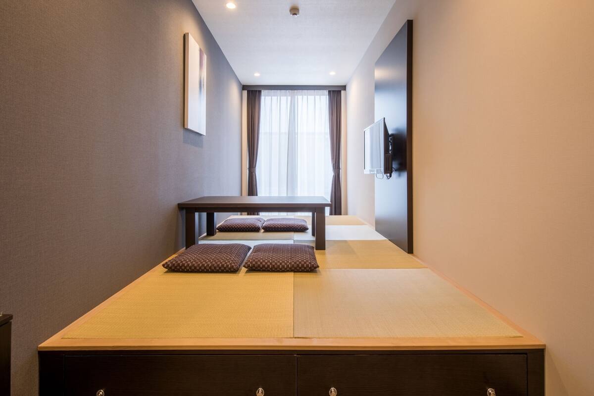 A modern hotel room with a bed, a TV mounted on the wall, and a window with curtains.