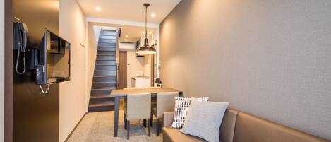 Una habitación de hotel compacta con sofá, una mesa de comedor, una pequeña cocina y una escalera.