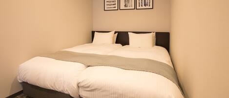 A neatly made bed with a gray headboard, a patterned throw blanket, and a plain wall with three framed pictures.
