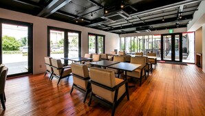 A spacious indoor area with wooden flooring, multiple tables and chairs, large windows, and a modern industrial ceiling design. - HOTEL R9 Kujukuri (Ichinomiya)