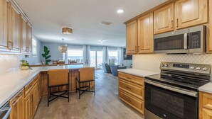 A modern kitchen with wooden cabinets, stainless steel appliances, and a large island with bar stools. - Spacious Beachfront Condo NEWLY REMODELED (Jacksonville Beach)