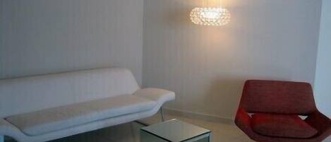 A modern living room with a white sofa, a red chair, and a glass coffee table.