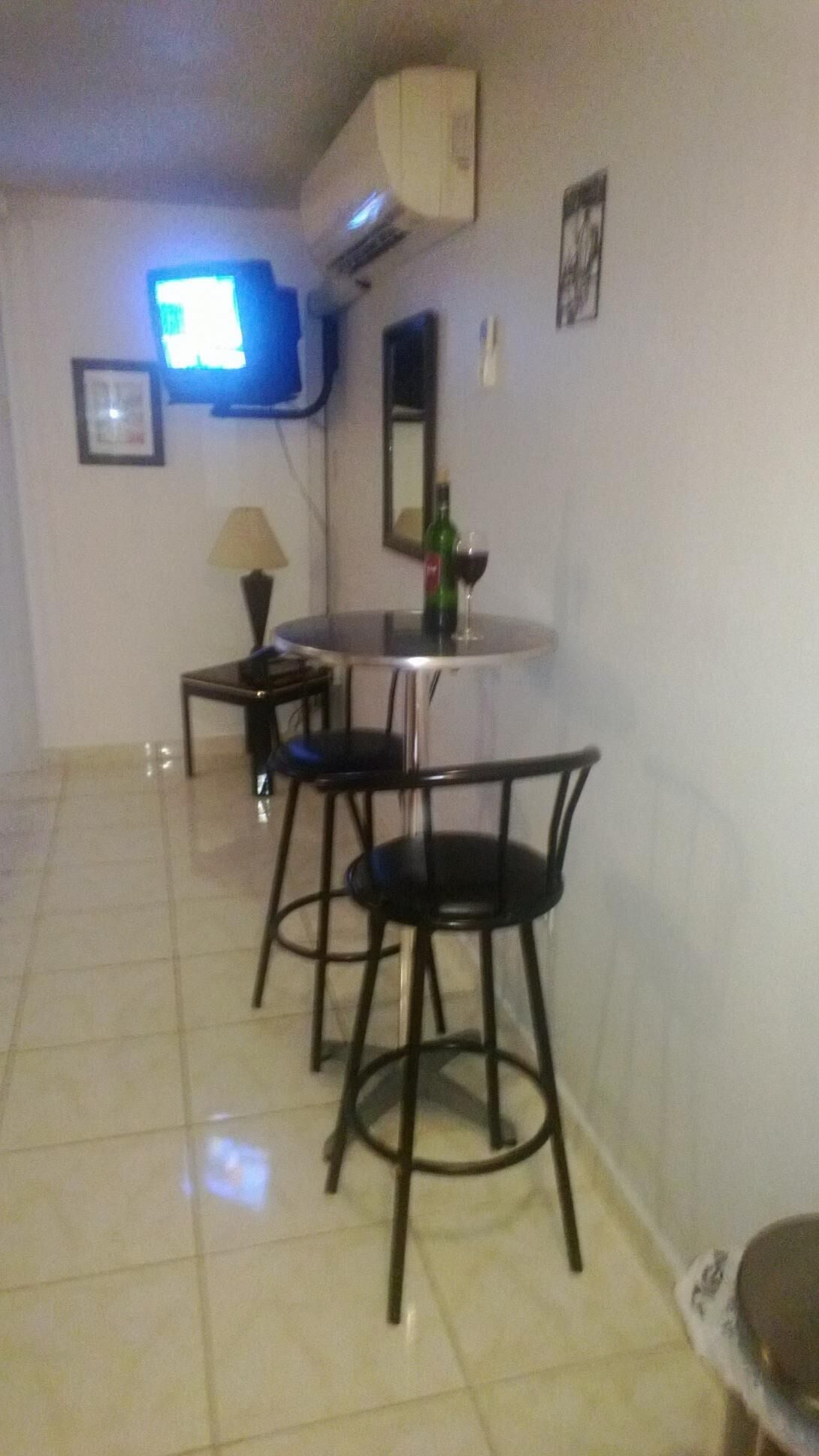 Een klein zithoekje met een ronde tafel en twee stoelen, een aan de muur bevestigde televisie en een spiegel.