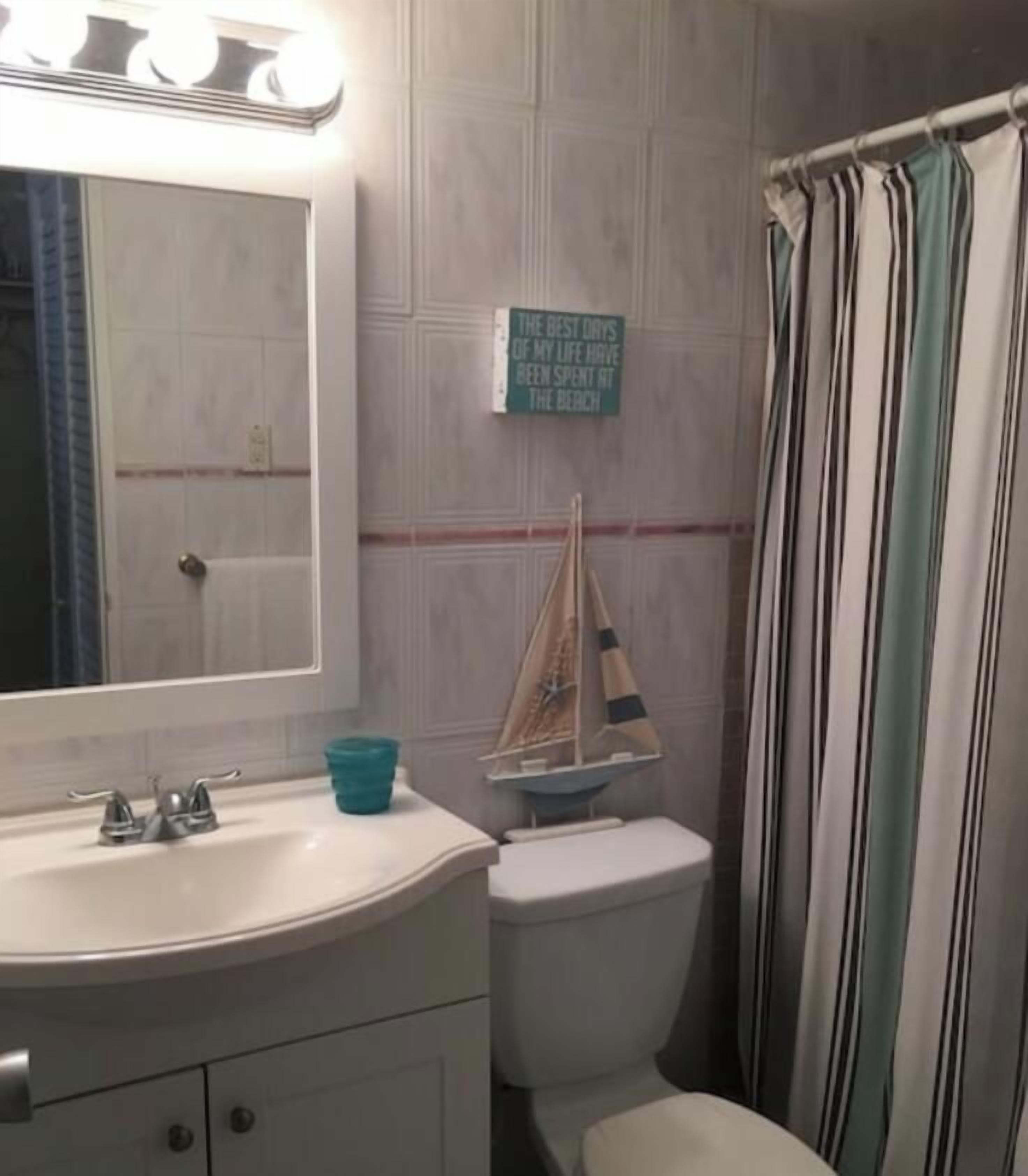 A bathroom with a white sink, a toilet, a striped shower curtain, and a small sailboat decoration on the wall.