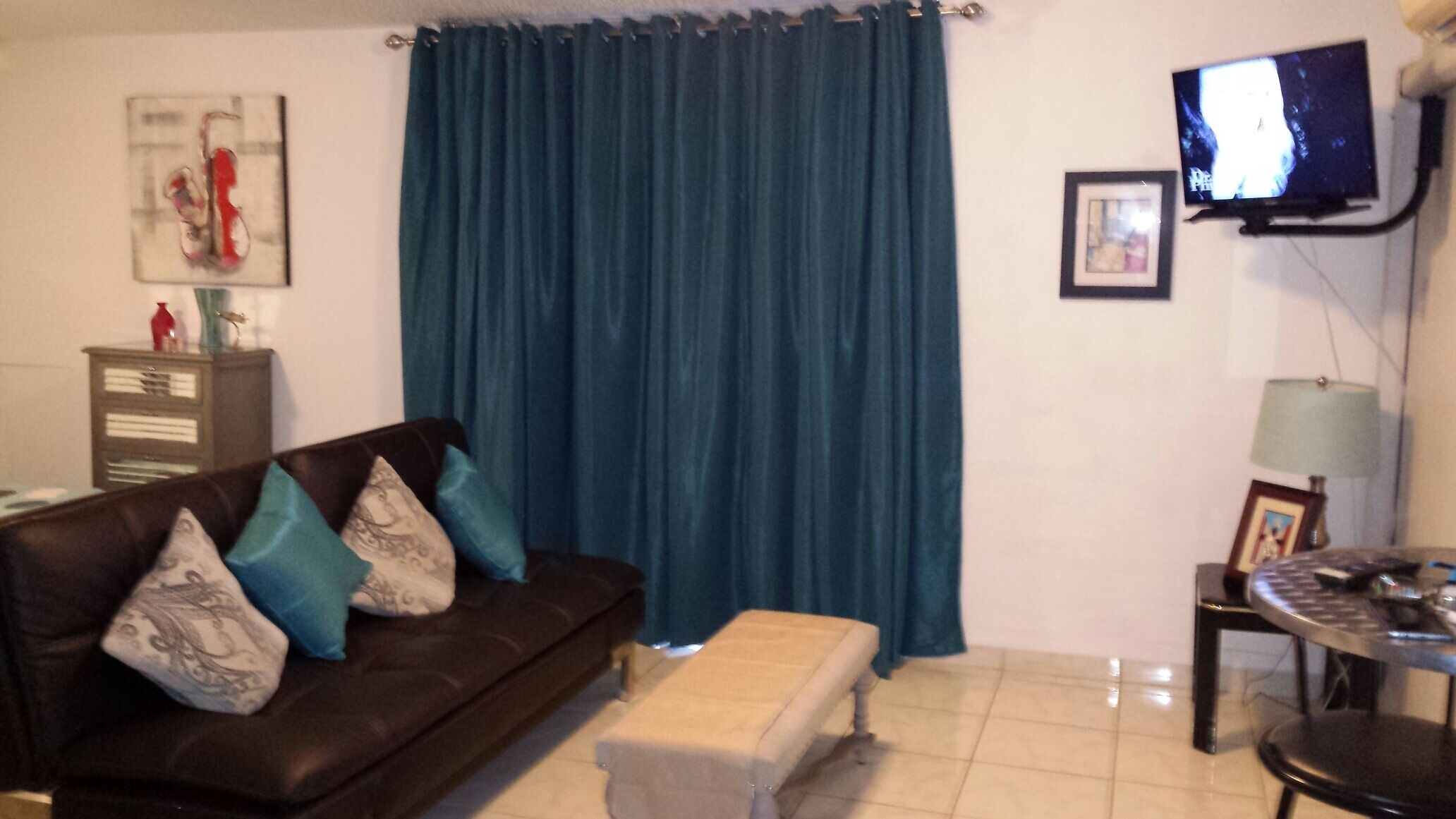 A living room with a brown sofa, teal curtains, a television, and a small table with a lamp.