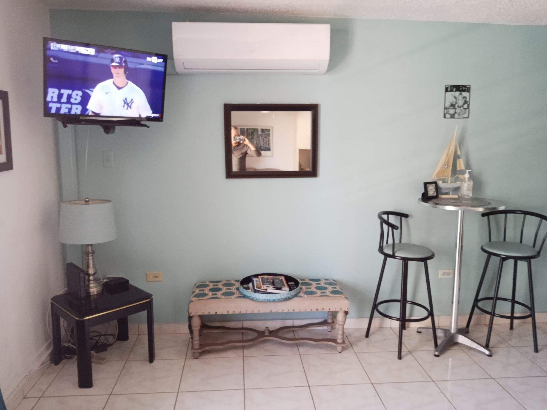 A living room with a TV, a bench, two chairs, and a small table.