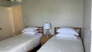 Una habitación con dos camas individuales, un ventilador de techo, una mesita de noche con lámpara y una puerta.