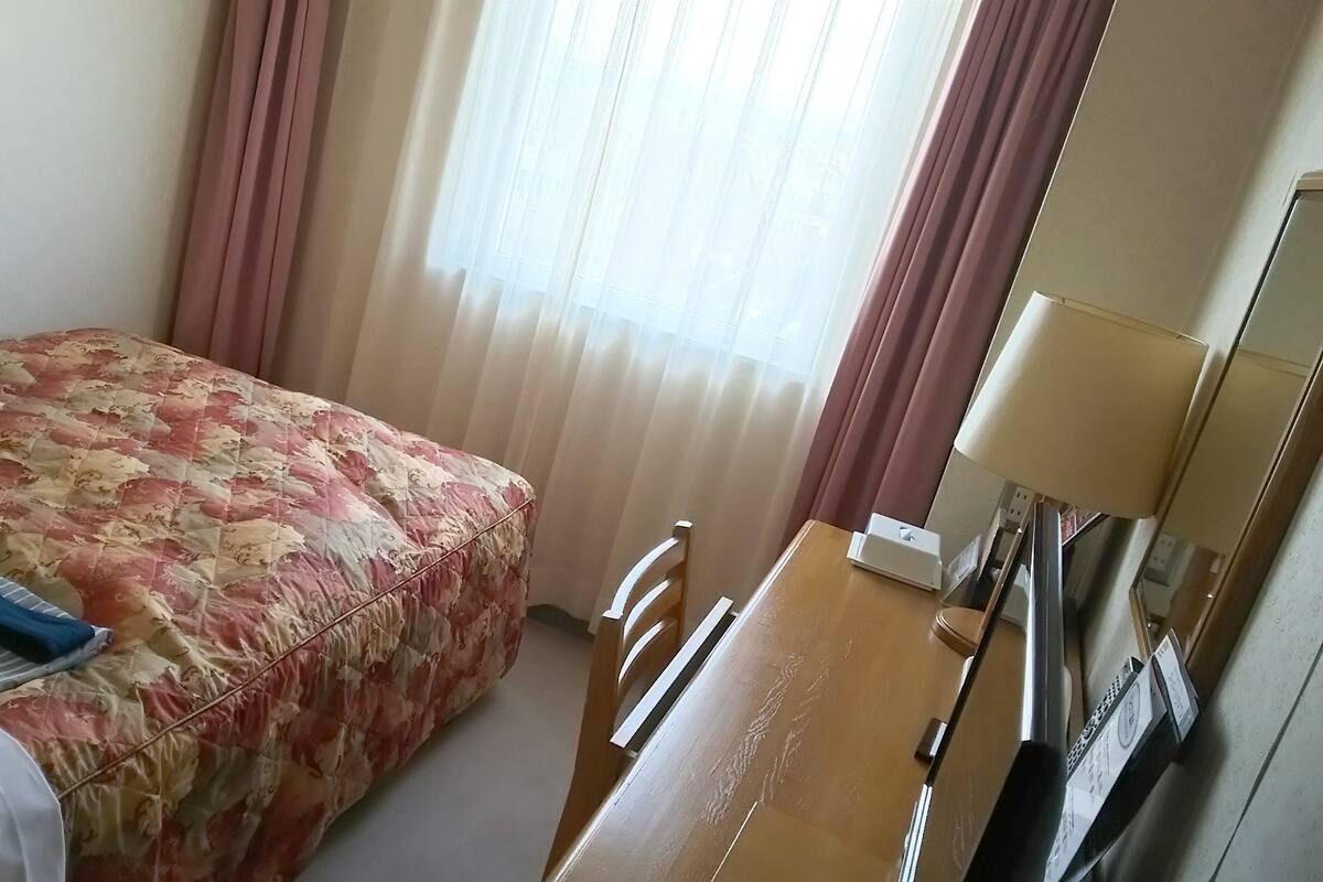 Une chambre d’hôtel avec un lit, un bureau, une lampe et une fenêtre avec des rideaux.