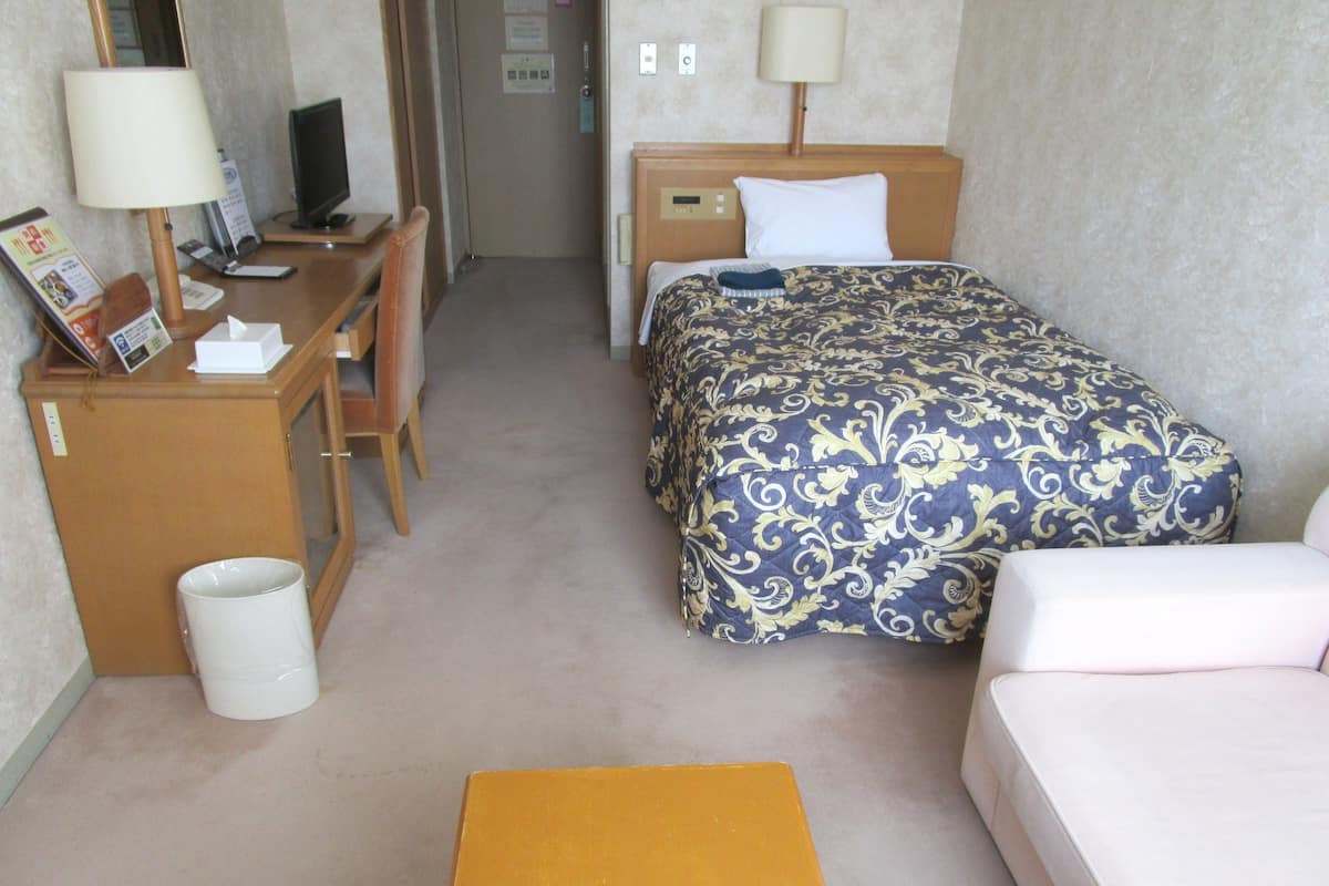 Une chambre d’hôtel avec un lit, un bureau, une chaise, un ordinateur et une petite table.