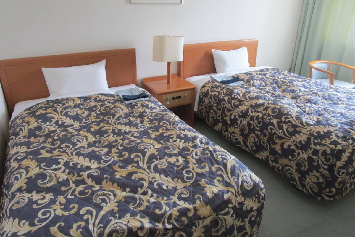 Deux lits simples avec des têtes de lit et des pieds de lit assortis, une table de chevet avec une lampe, et un tableau encadré accroché au mur.