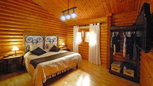 Une chambre située dans une cabane en rondins, avec un lit en bois, une table de chevet avec une lampe, une commode et un miroir.